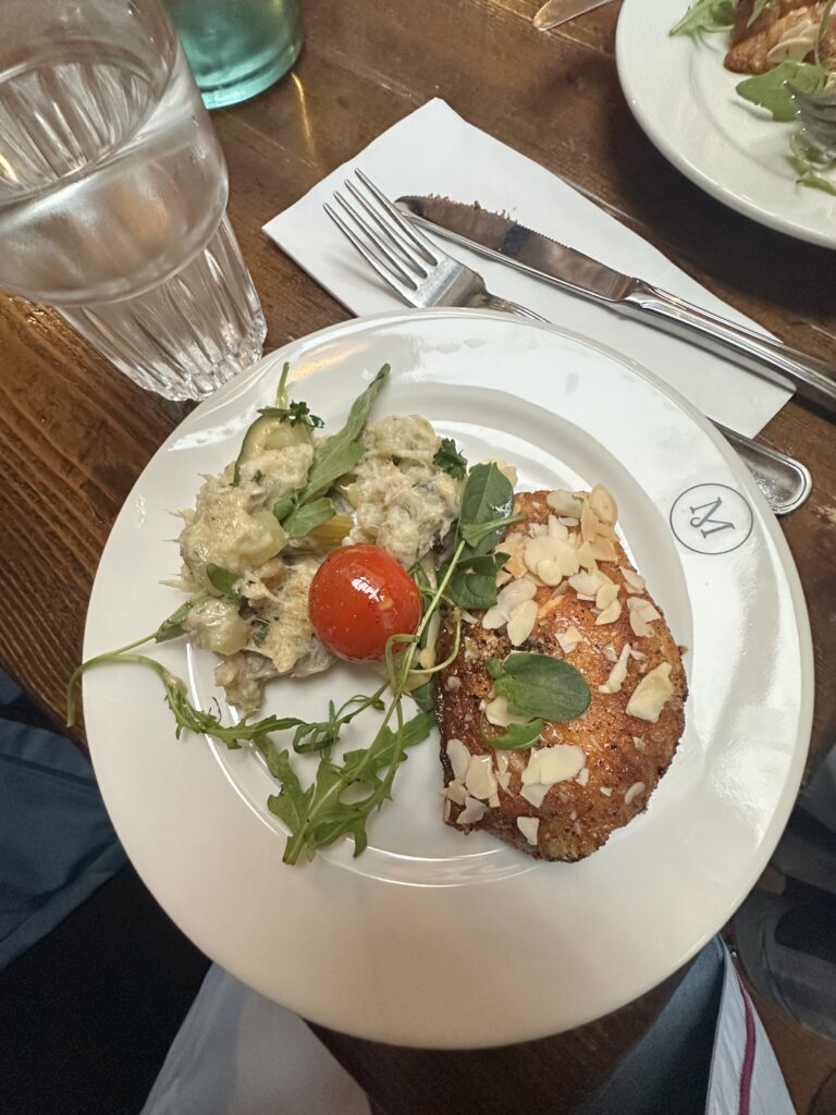 A fish entrée topped with almonds and served with a of potatoes and veggies on a white plate 