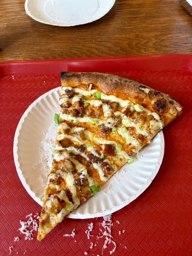 Slice of buffalo chicken pizza on a paper plate and red tray. 
